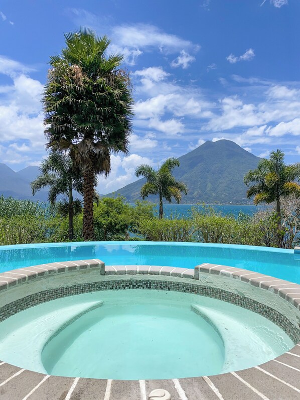 Una piscina con borde de azulejos, rodeada de palmeras y montañas al fondo.