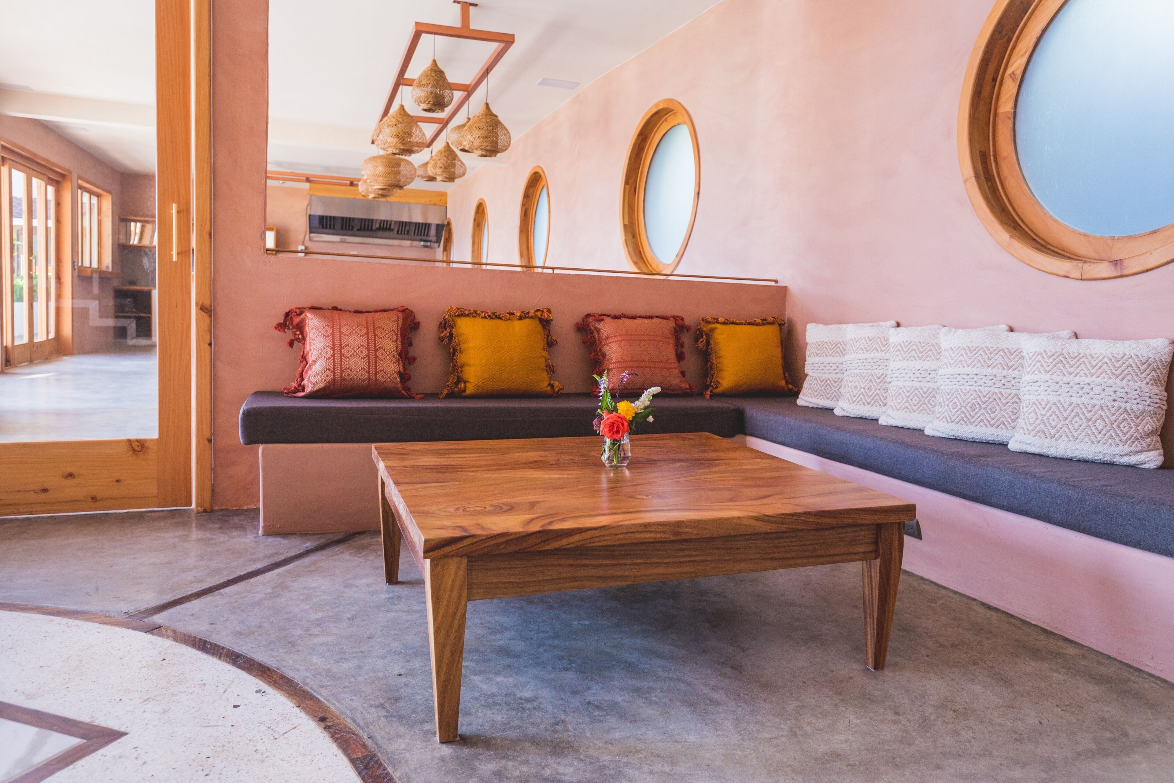 A modern interior with a wooden coffee table, a sofa with patterned cushions, and a large mirror on the wall.