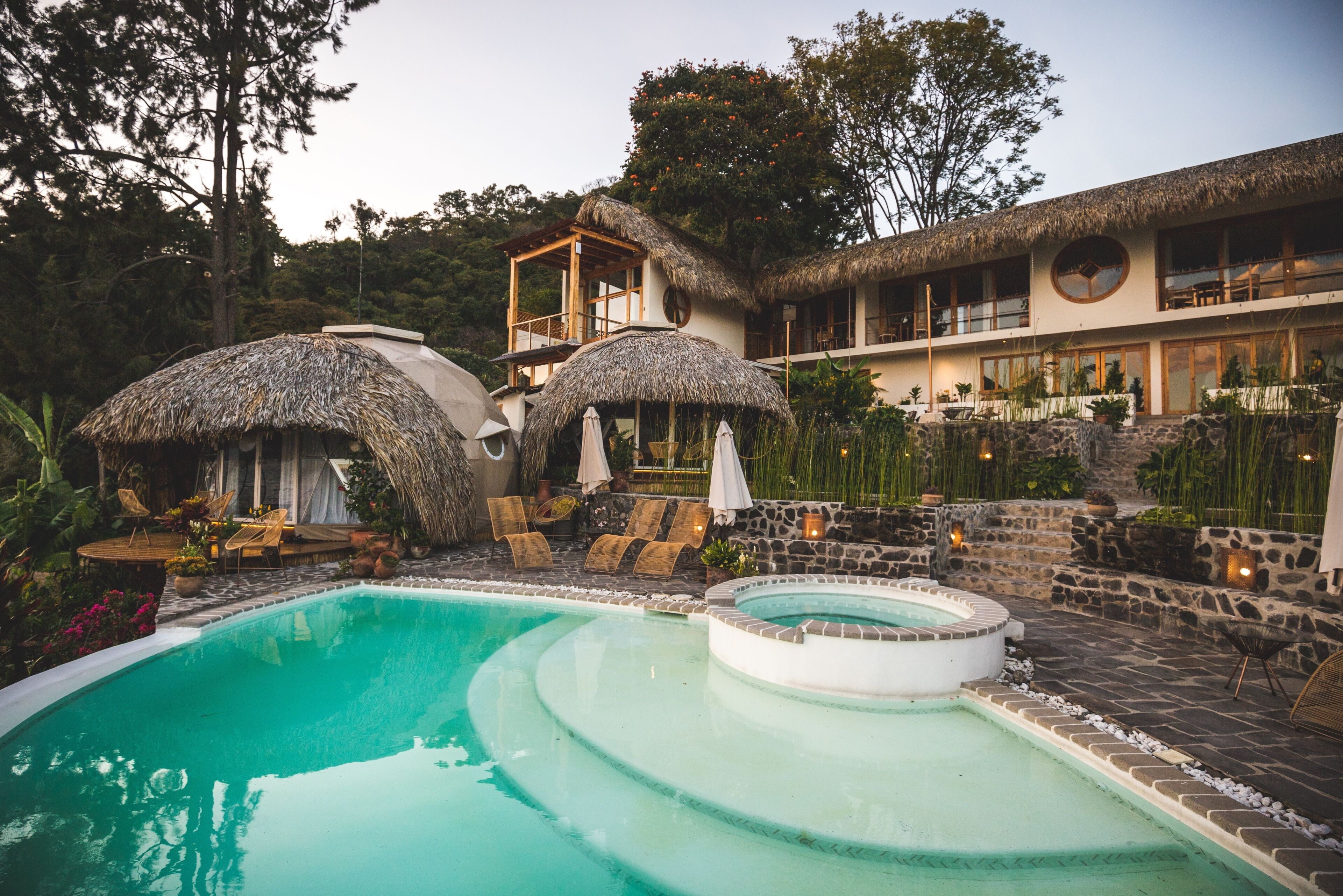 A pool area with a hot tub, lounge chairs, and thatched umbrellas.