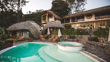 A pool area with a hot tub, lounge chairs, and thatched umbrellas.