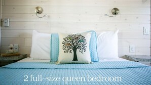 A 2 full-size queen bedroom with a blue quilted bedspread, white pillows, and a tree design pillow.