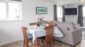 A cozy living area with a dining table, chairs, a sofa, and a TV. - Duart At The Sea (Wick)