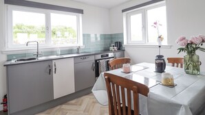 A modern kitchen with two windows, a dining table with chairs, and a vase with flowers. - Duart At The Sea (Wick)