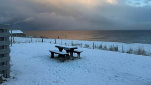 A snowy beach with a bench and a building in the foreground. - Duart At The Sea (Wick)