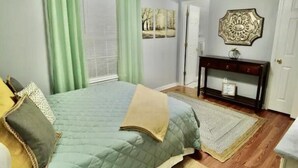 Een slaapkamer met een bed, nachtkastje, spiegel en een deur.