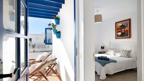 Een slaapkamer met een bed, kussens, een schilderij en een balkon met stoelen en plantenpotten.