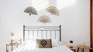 Een net opgemaakt bed met een kussen met dessin, een nachtkastje met een lamp, en wandventilatoren.
