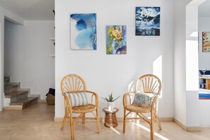 A room with two wicker chairs, a small table with a plant, and artwork on the wall.