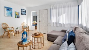 Een woonkamer met een bank, twee stoelen, een kleine tafel met een lantaarn en kunst aan de muur.