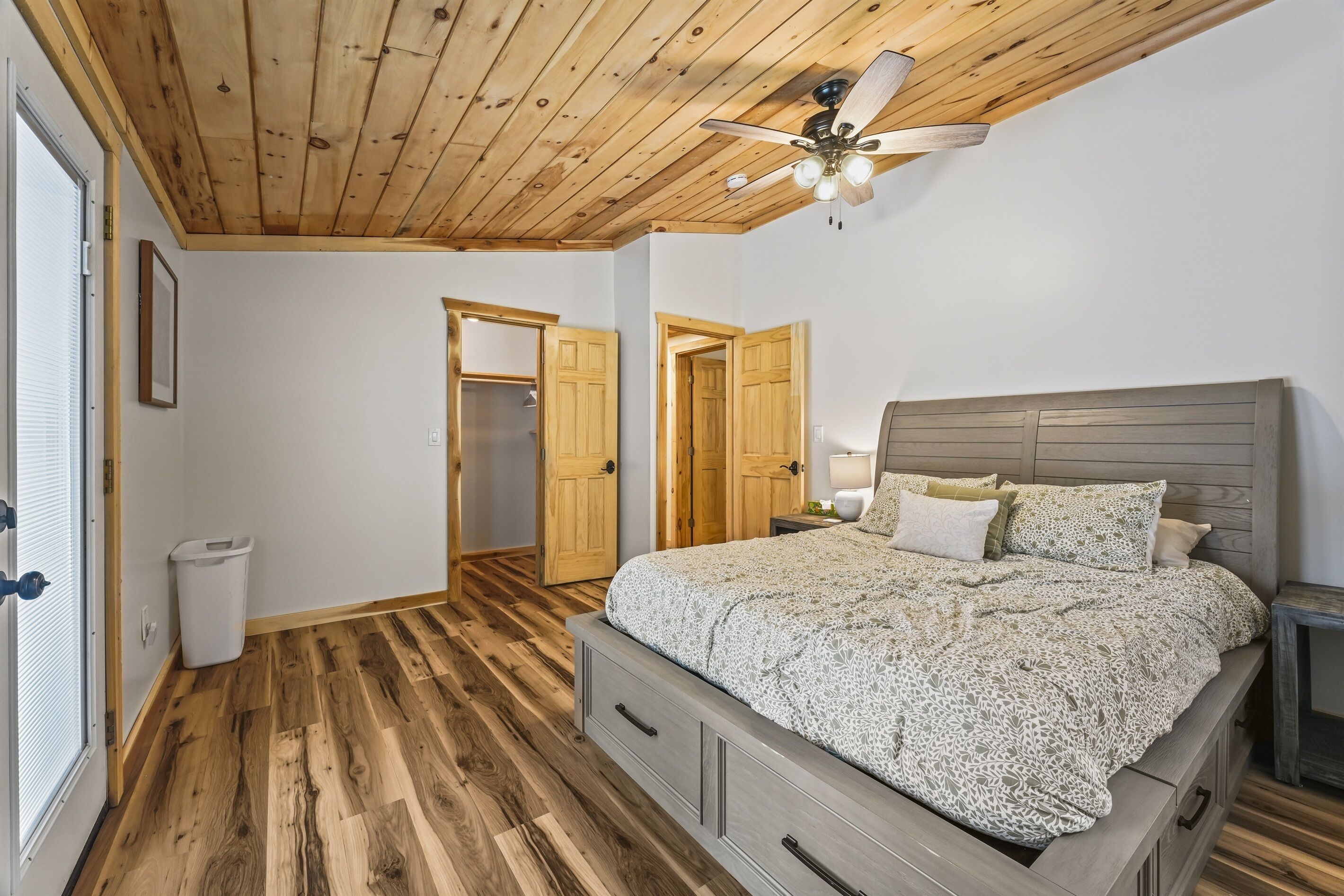 Una camera da letto con soffitto in legno, un letto con copripiumino decorato, un comodino e una ventola a soffitto.