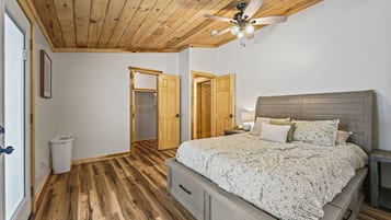 Una camera da letto con soffitto in legno, un letto con copripiumino decorato, un comodino e una ventola a soffitto.