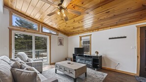 Ein geräumiges Wohnzimmer mit Holzboden, einem großen Fenster, einer Couch, einem Couchtisch und einem Fernseher.