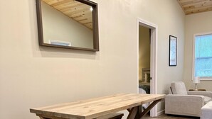 Una mesa de madera con bancos en una habitación con piso de madera, techo con vigas a la vista y un cuadro en la pared.