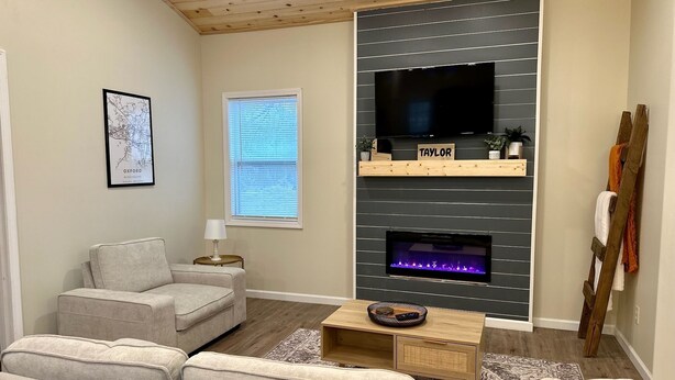 Una sala de estar con chimenea gris, un televisor de pantalla plana, un sofá y una escalera de madera apoyada en la pared.