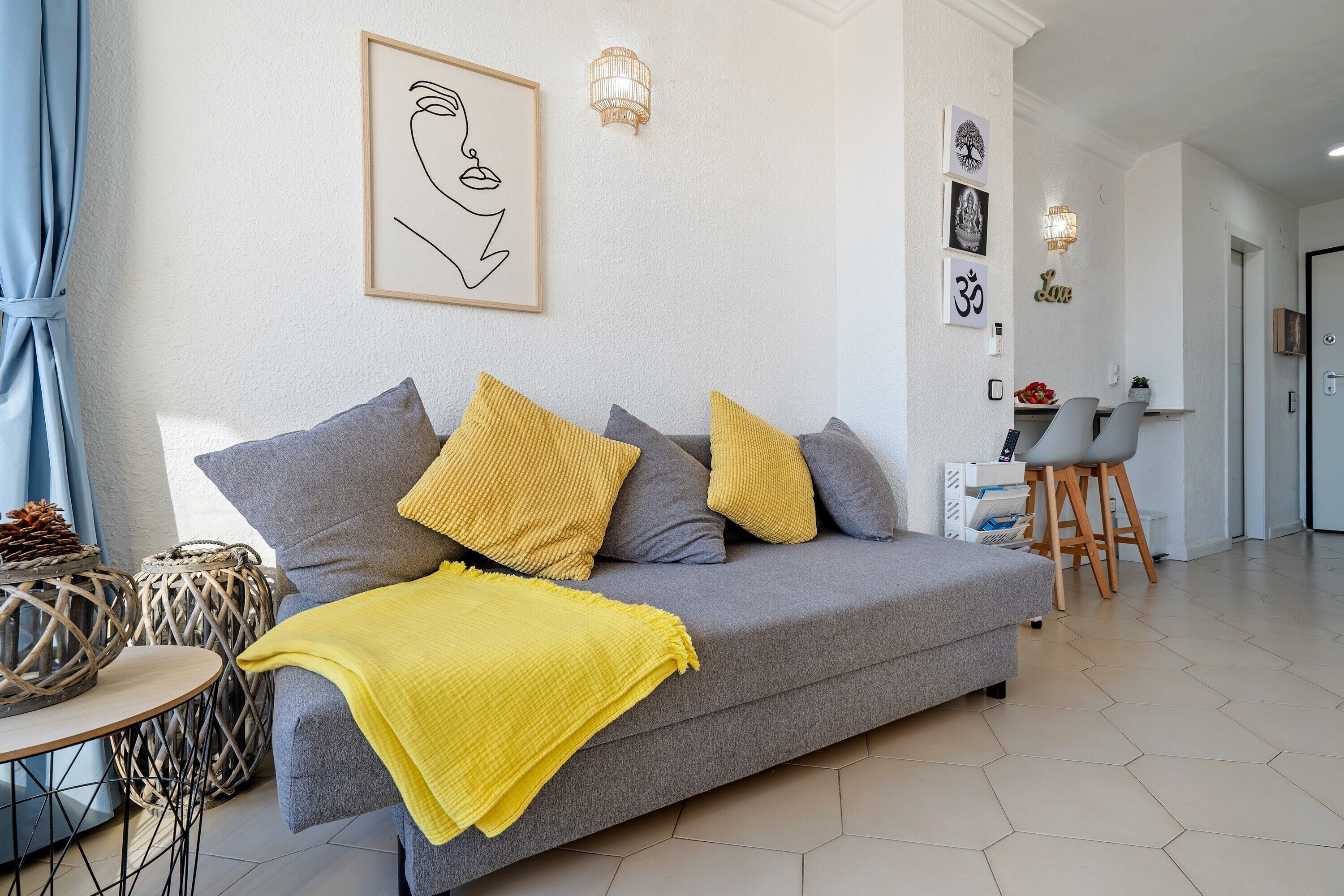 A modern living room with a grey sofa, yellow and grey cushions, a yellow throw blanket, and a framed abstract artwork on the wall.