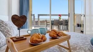 A balcony with a view of the sea, a wooden tray with croissants and a heart-shaped decoration, and a table with chairs. - 'Salou Beach' Apartment with Sea View, Wi-Fi and Air Conditioning (Salou)