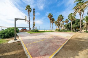 An outdoor basketball court with a basketball hoop, palm trees, and a clear sky.