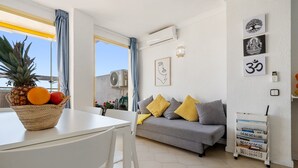 A living room with a grey sofa, a white table, a basket of fruit, and wall art. - 'Salou Beach' Apartment with Sea View, Wi-Fi and Air Conditioning (Salou)