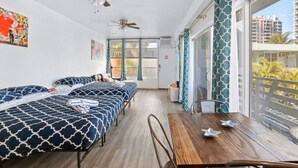 Une chambre d’hôtel avec un balcon, deux lits avec une literie à motifs, une table en bois et des ventilateurs de plafond.
