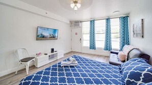 Ein Schlafzimmer mit einem Bett, einem Sessel, einem Schreibtisch und einem Fenster mit Vorhängen.