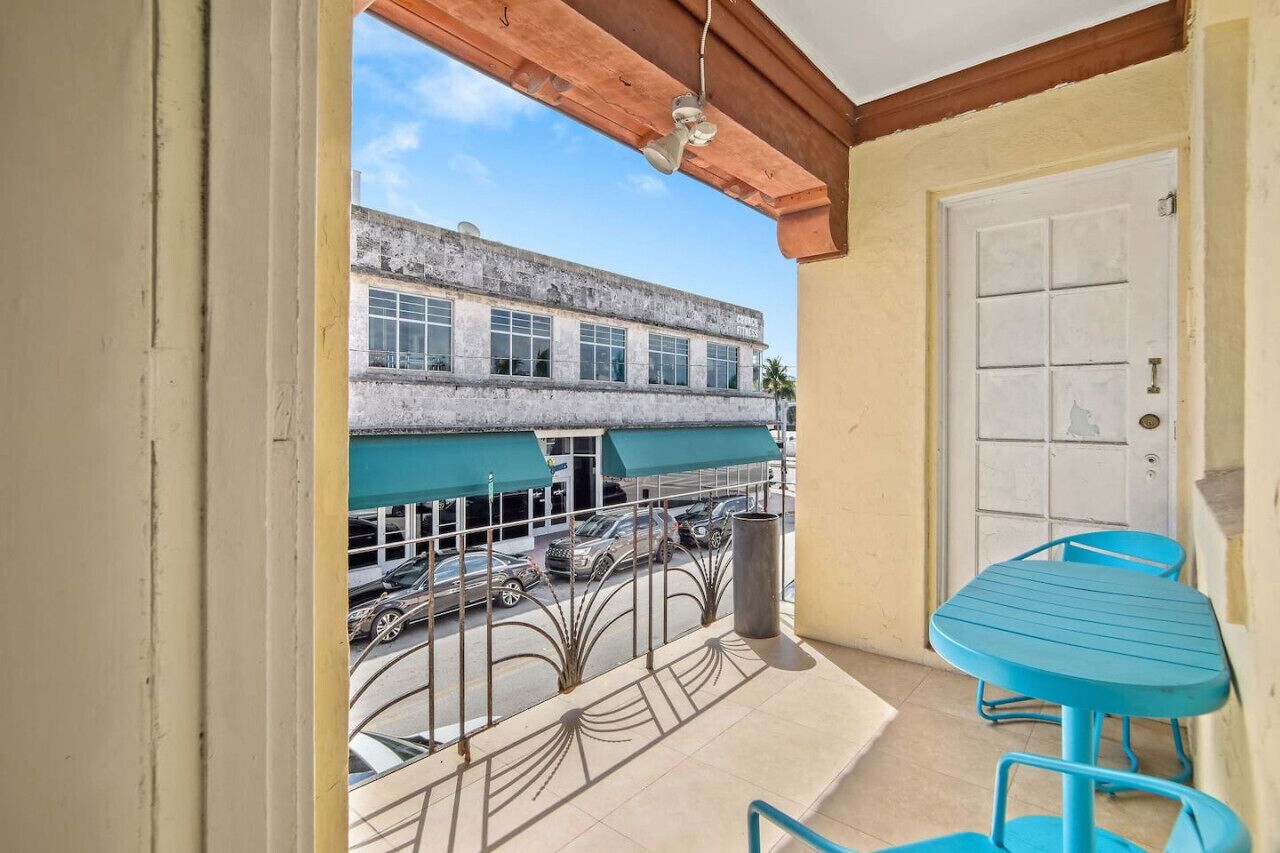 A balcony with a table and chairs, a view of a building across the street, and a door to the right.