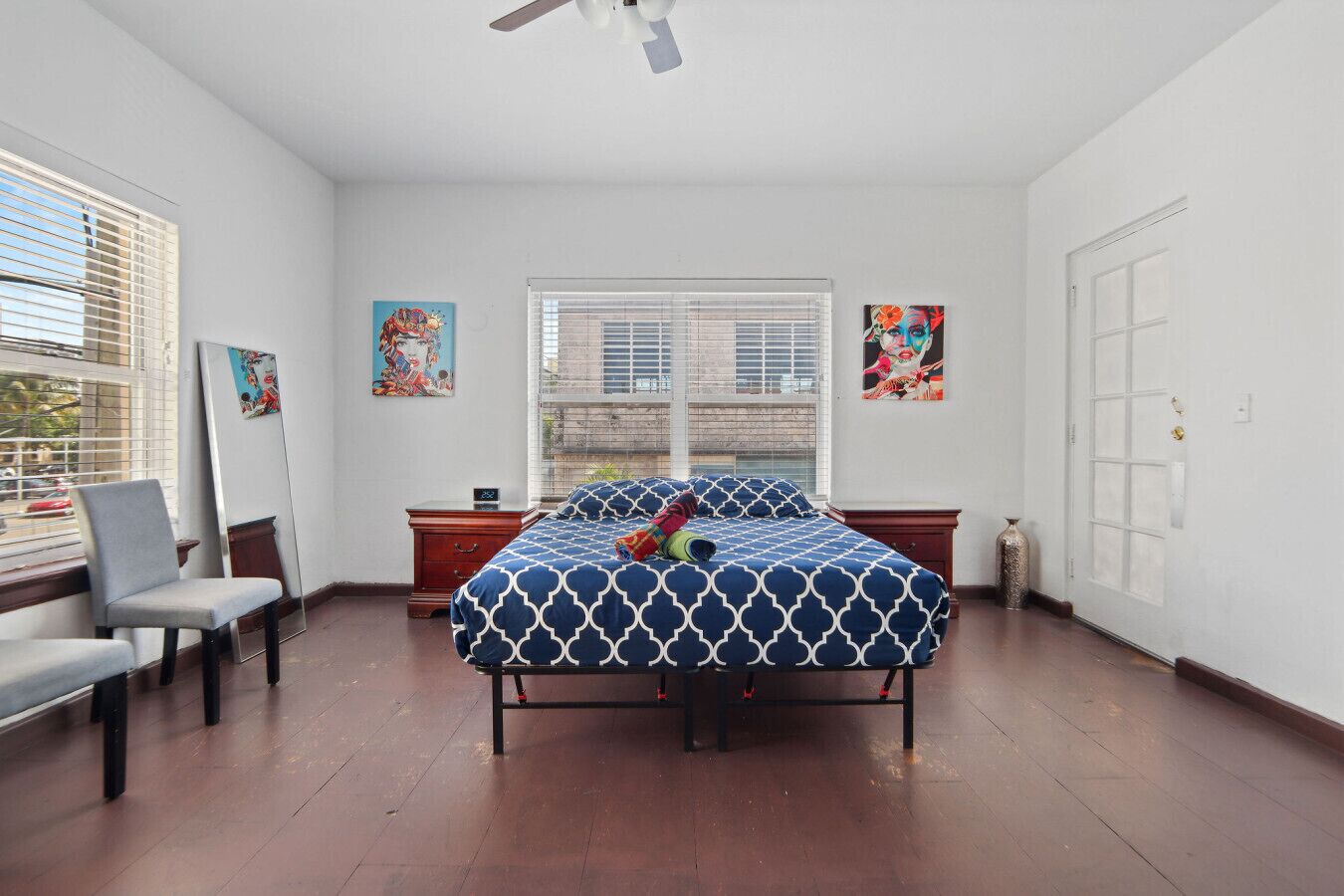 A bedroom with a bed, a chair, a nightstand, a window, and artwork on the walls.