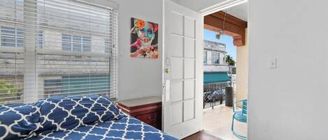 Une chambre à coucher avec un lit, une table de chevet, un tableau et une vue sur le balcon extérieur.
