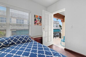 Un dormitorio con cama, mesita de noche, un cuadro y vistas al balcón exterior.