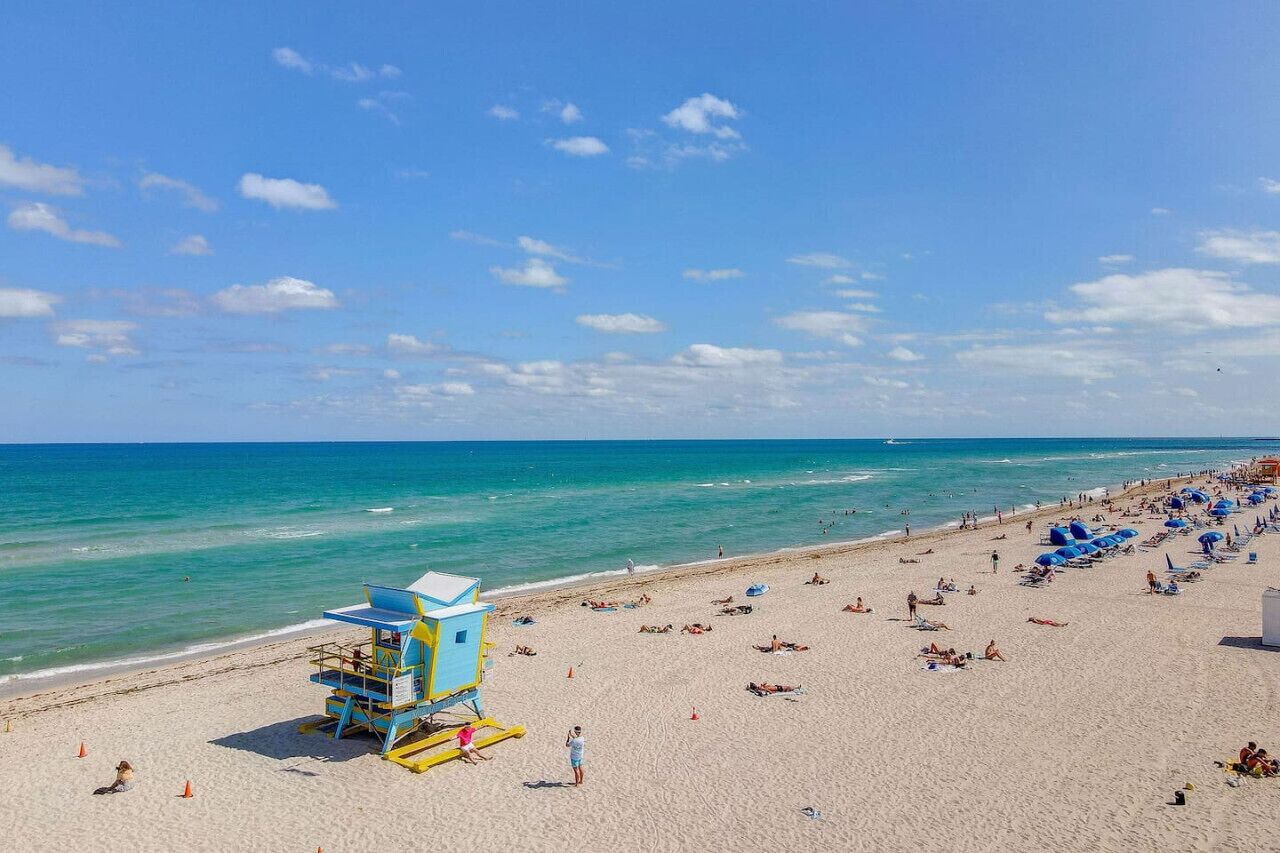 A beach with lifeguard towers, umbrellas, and people relaxing.
