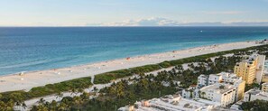 A beachside view with a sandy beach, palm trees, and buildings in the foreground. - Fresh Ocean Dr, Apt w/2 Queen Beds-Steps 2 Beach (Miami Beach)