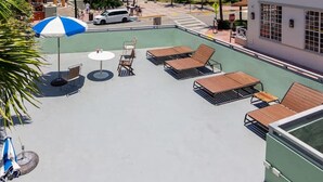 A rooftop pool area with lounge chairs and umbrellas, surrounded by palm trees and a cityscape. - Deco Apt w/2 Queen Beds on Ocean Dr, South Beach (Miami Beach)