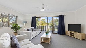 A modern living room with a sofa, coffee table, TV, and balcony with curtains. - Generous Family Home with 4 Bedrooms, Pool, Pet Friendly (Sunshine Beach)