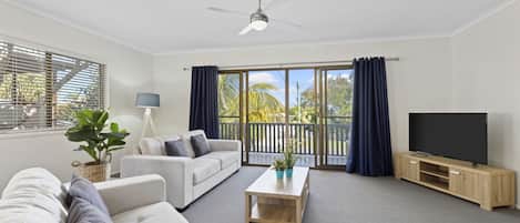 A modern living room with a sofa, coffee table, TV, and balcony with curtains.