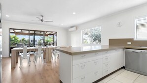 A modern kitchen with a central island, white cabinetry, and a built-in dishwasher. - Generous Family Home with 4 Bedrooms, Pool, Pet Friendly (Sunshine Beach)