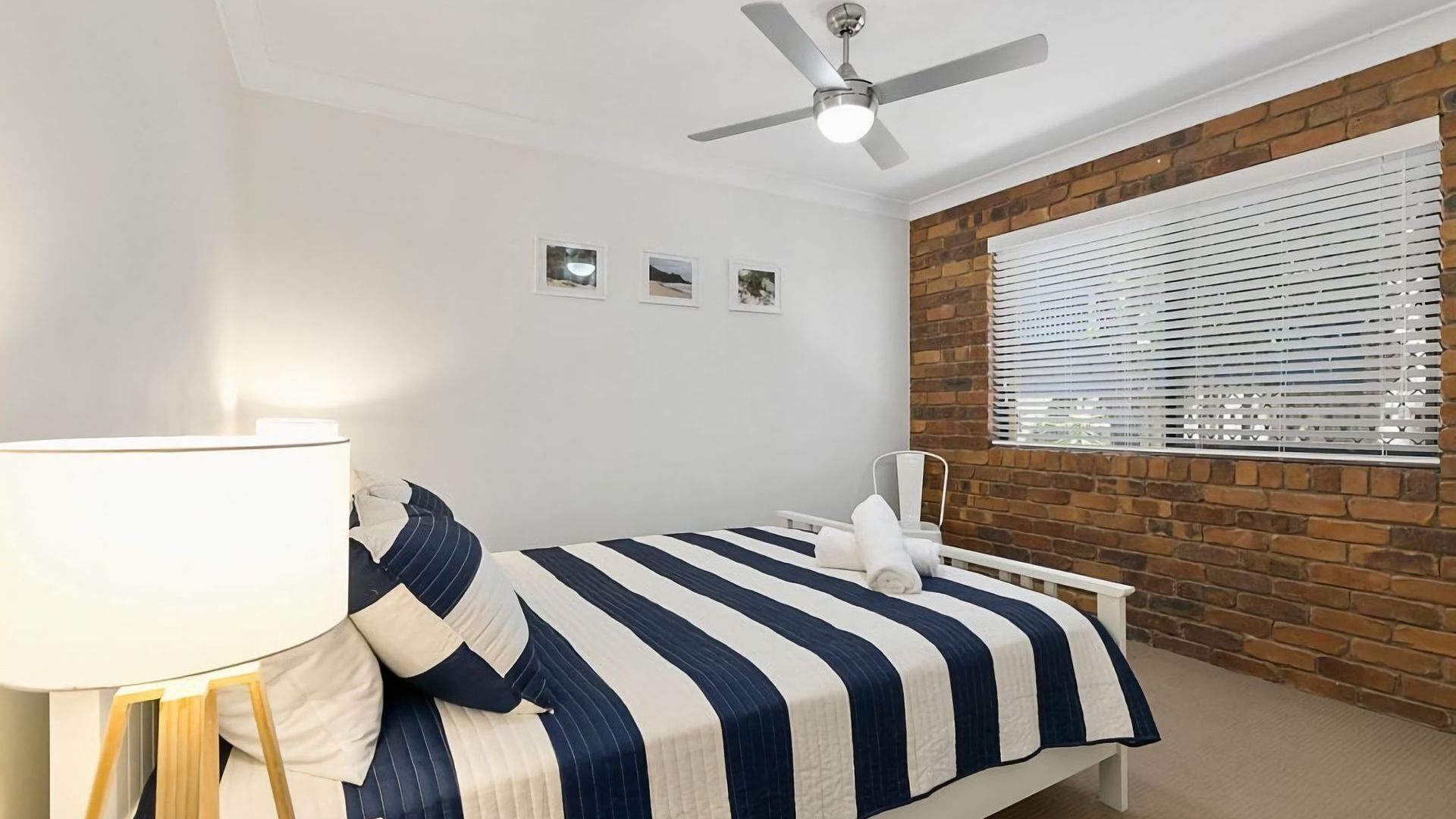 A bedroom with a bed, a bedside table with a lamp, a ceiling fan, and a window with blinds.