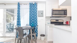 Cocina compacta equipada con microondas, tostadora y estufa. Hay un comedor con mesa y sillas, y se observa un cubo de basura.