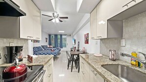 A modern kitchen with a central island, a dining area with a sofa, and a large window.