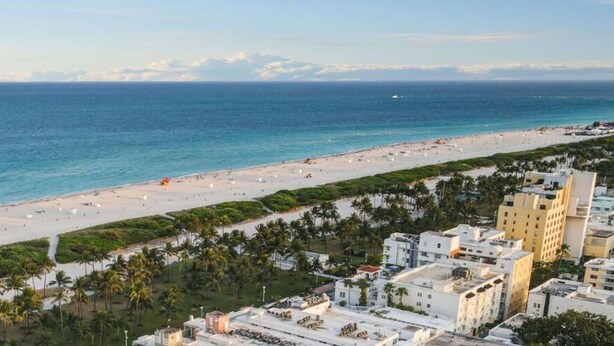 A coastal cityscape with a beach, palm-lined promenade, and modern buildings.