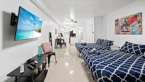 A modern hotel room with a large bed, a desk with a chair, a TV mounted on the wall, and a colorful artwork on the wall.