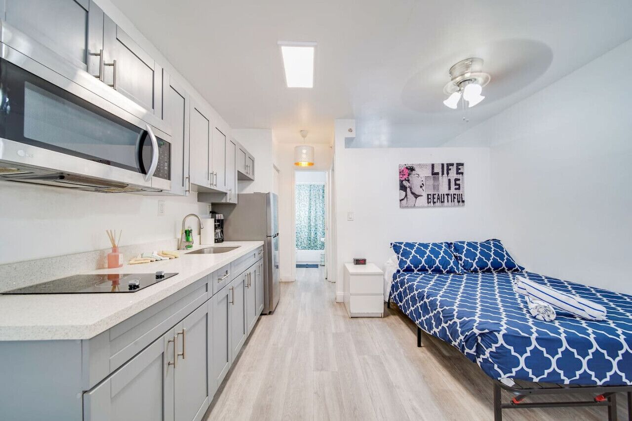 Una habitación de hotel compacta con kitchenette, una cama con ropa de cama estampada y una cita motivacional en la pared.