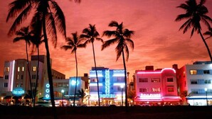 A hotel with a neon sign, palm trees, and a sunset sky. - Ocean Drive Beach Fun, w/2 Queen Beds South Beach (Miami Beach)
