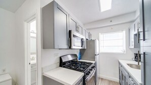 A modern kitchen with grey cabinets, a stainless steel range, and a window providing natural light. - Ocean Drive Beach Fun, w/2 Queen Beds South Beach (Miami Beach)
