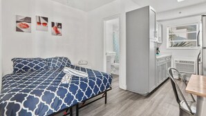 Habitación de hotel compacta con cama, kitchenette y ventilador de techo.