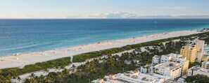A coastal view with a beach, palm trees, and buildings. - Stylish Ocean Dr Apt w/ 2 Queen Beds, Across Beach (Miami Beach)