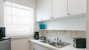 Eine kompakte Küche mit weißen Schränken, einer Spüle, einer Kaffeemaschine und einem Toaster.