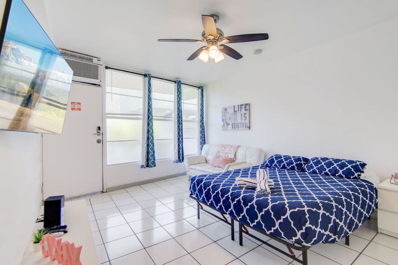 A bedroom with a bed, a ceiling fan, a window with curtains, and a wall with a poster.