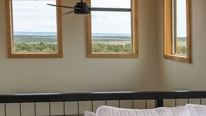 Une chambre à coucher avec un lit, un ventilateur de plafond et deux fenêtres donnant sur le paysage.