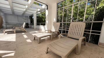 Un’area salotto esterna illuminata dal sole, con poltrone relax e una pergola.
