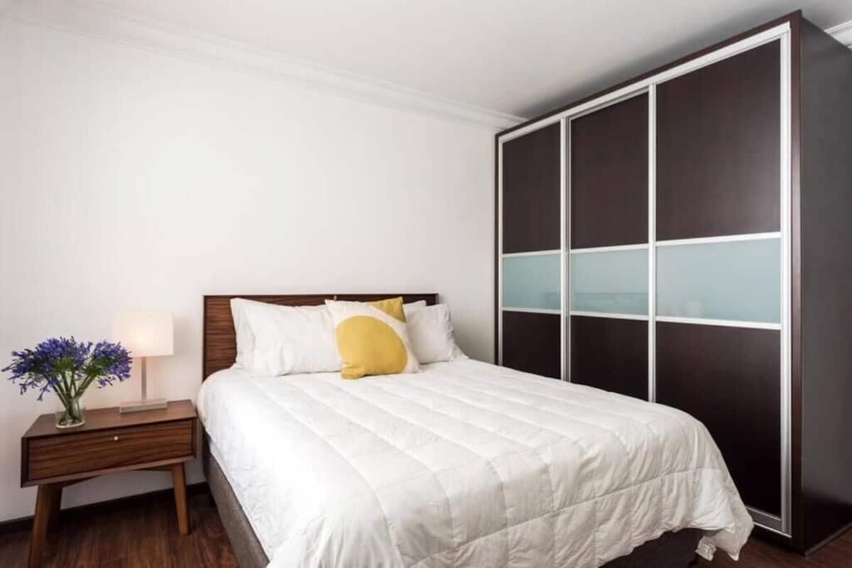 Ein ordentlich eingerichtetes Schlafzimmer mit Bett, Nachttisch, Lampe und Kleiderschrank.