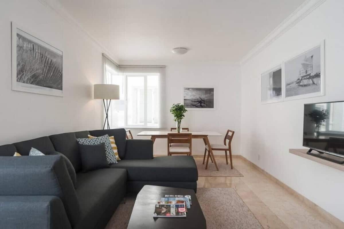 Ein modernes Wohnzimmer mit einer Couch, einem Couchtisch, einem Fernseher, einem Esstisch, Stühlen und Kunstwerken an den Wänden.